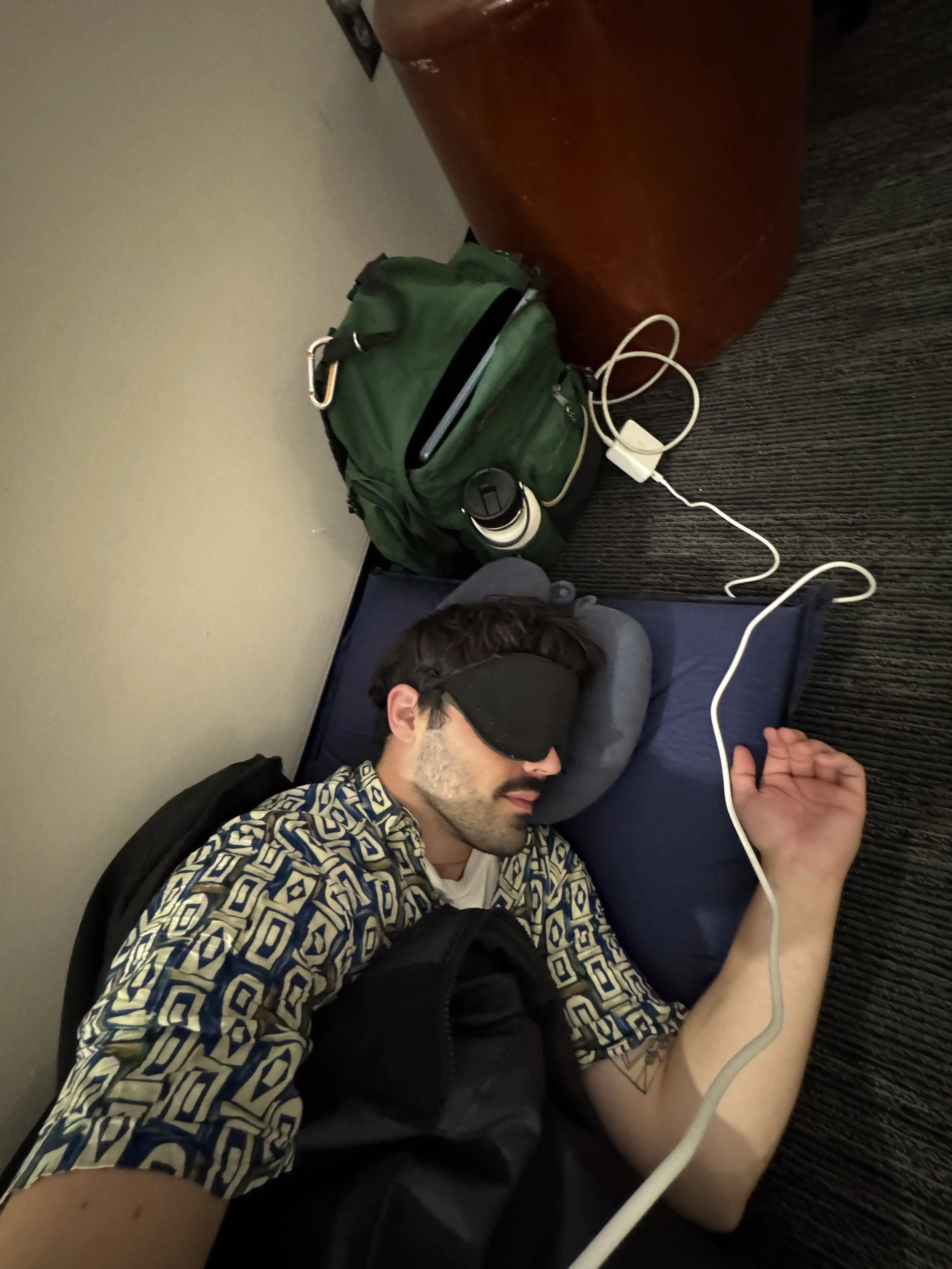 Man sleeping on floor with patterned shirt and eye mask.
